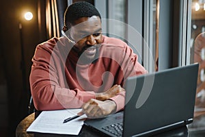 Cheerful young african american student man in headphones using computer in cafe. Online video chat with friends.