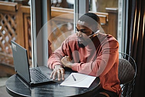 Cheerful young african american student man in headphones using computer in cafe. Online video chat with friends.