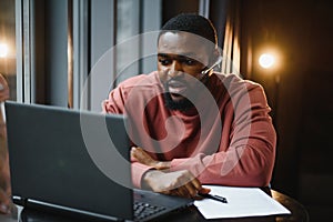 Cheerful young african american student man in headphones using computer in cafe. Online video chat with friends