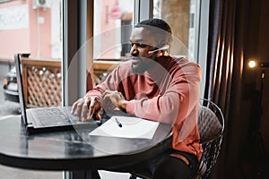Cheerful young african american student man in headphones using computer in cafe. Online video chat with friends.
