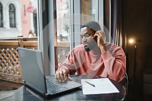 Cheerful young african american student man in headphones using computer in cafe. Online video chat with friends.