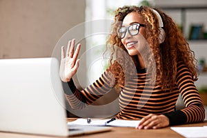 Cheerful afro american female waving at webcam on laptop, having video call while working remotely or studying online