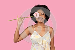 Cheerful young African American woman with a radiant smile, holding a pink gerbera daisy