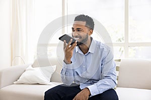 Cheerful young African man dictating voice message on smartphone speaker