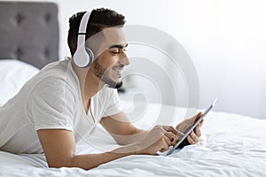 Cheerful Young Arab Man Relaxing With Digital Tablet In Bed