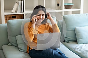 Cheerful Young Arab Woman Talking On Cellphone And Using Laptop At Home