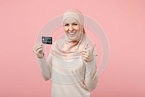 Cheerful young arabian muslim woman in hijab light clothes posing isolated on pink background. People religious Islam