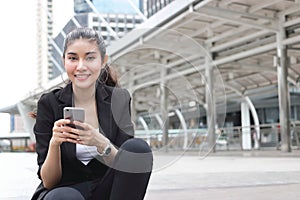 Cheerful young Asian business woman with mobile smart phone in urban background.