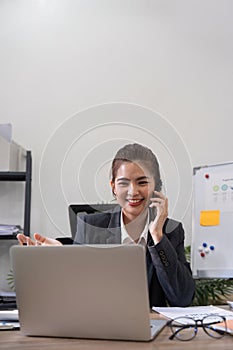 Cheerful young asian business woman talking on phone working in office. Happy positive Asian businesswoman company