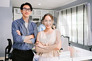 Cheerful young Asian businessman wearing eyeglasses and a businesswoman in casual smiling and looking at the camera while standing