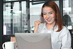 Cheerful young Asian businesswoman with laptop having ideas in office. Thinking and thoughtful business concept.