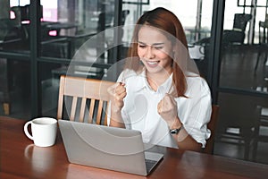 Cheerful young Asian businesswoman with laptop smiling on the workplace in office. Successful business concept.