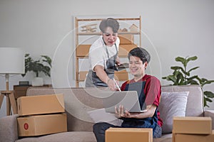 A cheerful young Asian gay couple checks their online product orders on a tablet and celebrates their orders success