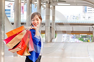 Cheerful young Asian woman carrying shopping bags while walking along the street. Shopping concepts