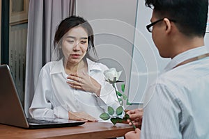 Cheerful young Asian woman excited to get a white rose in office on valentine`s day. Love and romance in workplace concept.