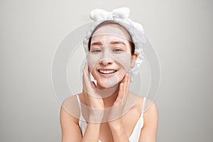 Cheerful young Asian woman with facial clay mask isolated on white background