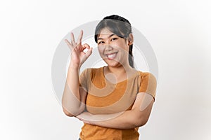 The cheerful young Asian woman smiling and showing the OK hand sign standing on white background