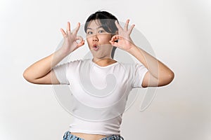 The cheerful young Asian woman smiling and showing the OK hand sign standing on white background