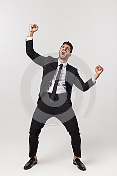 Cheerful young bearded business man show hand up excited with clenched fists. Full length portrait business man isolated