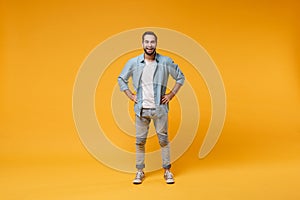 Cheerful young bearded man in casual blue shirt posing isolated on yellow orange background, studio portrait. People