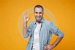 Cheerful young bearded man in casual blue shirt posing isolated on yellow orange wall background studio portrait. People