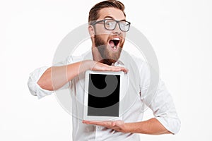 Cheerful young bearded man showing display of tablet computer.