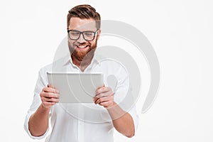 Cheerful young bearded man using tablet computer.