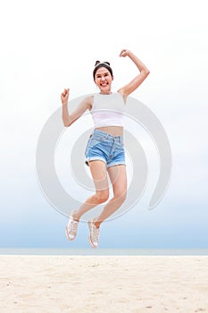 Cheerful young beautiful Asian woman having fun in white shirt and shorts jumping high on the beach.