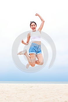 Cheerful young beautiful Asian woman having fun in white shirt and shorts jumping high on the beach.