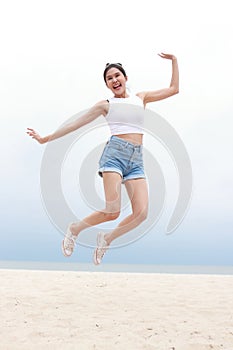 Cheerful young beautiful Asian woman having fun in white shirt and shorts jumping high on the beach.