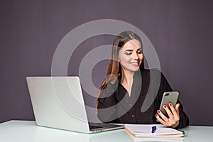 Cheerful young beautiful woman in glasses use mobile phone and using laptop with smile while sitting at her working place