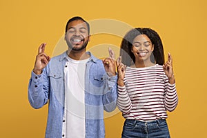 Cheerful Young Black Couple Crossing Fingers, Making Wish With Closed Eyes