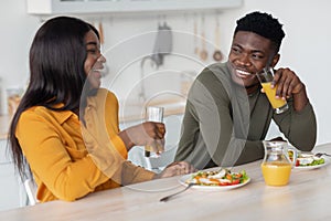 Cheerful young black couple sitting at table and eating tasty breakfast together