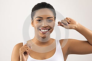 Cheerful young black woman flossing mouth, showing white teeth