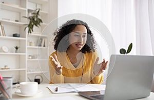 Cheerful young black woman in headphones making video call on laptop at home