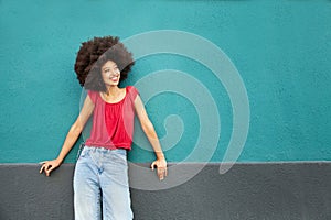 Cheerful young black woman standing against blue wall in daylight. Lifestyle concept