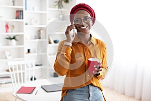 Cheerful young black woman talking on phone, having coffee break