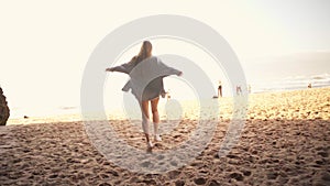 Cheerful young blond woman running on sandy beach on sunny day