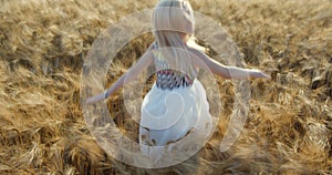 Cheerful young blonde woman with natural make-up and charming smile is resting in the golden field. She is spinning