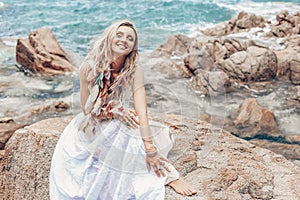 Cheerful young boho style woman in white dress on stone beach