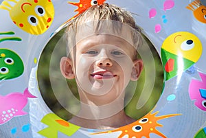 Cheerful young boy with joyful expression peeks through the center of colorful inflatable swim ring