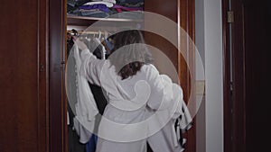 Cheerful young brunette girl dancing energetically holding hangers with clothes. Beautiful Caucasian woman in white