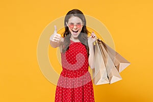 Cheerful young brunette woman girl in red summer dress, eyeglasses posing isolated on yellow background. People