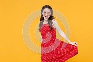 Cheerful young brunette woman girl in red summer dress, eyeglasses posing isolated on yellow wall background studio