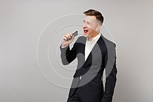 Cheerful young business man in black suit with wireless earphones listening music singing hold mobile phone isolated on