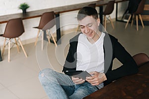 Cheerful young business man wearing casual fashion clothes sits at table and uses tablet.