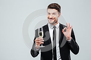 Cheerful young businessman drinking champagne and showing ok sign