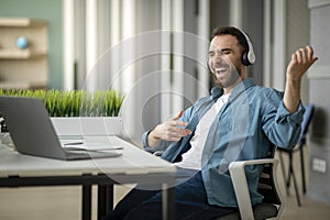 Cheerful young businessman having fun at workplace in office, playing virtual guitar