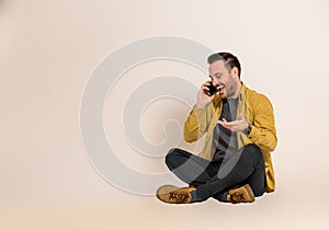 Cheerful young businessman laughing and communicating with client over smartphone while sitting with crossed legs. Sales manager