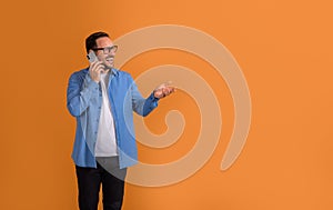 Cheerful young businessman looking away and discussing over mobile phone against orange background